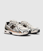 White and beige athletic sneakers with black and gold details on a neutral background