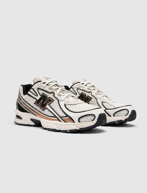 White and beige athletic sneakers with black and gold details on a neutral background
