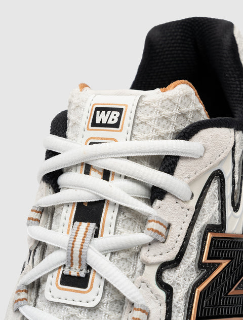 Close-up of white textured sneaker with black and gold accents, WB logo on tongue, streetwear style