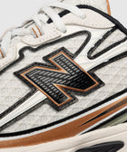 Close-up of white mesh sneaker with black and tan accents, textured logo, and white laces