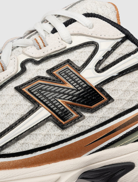 Close-up of white mesh sneaker with black and tan accents, textured logo, and white laces