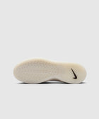 White sneaker outsole with textured grip and black swoosh logo on neutral background