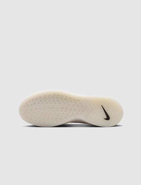 White sneaker outsole with textured grip and black swoosh logo on neutral background