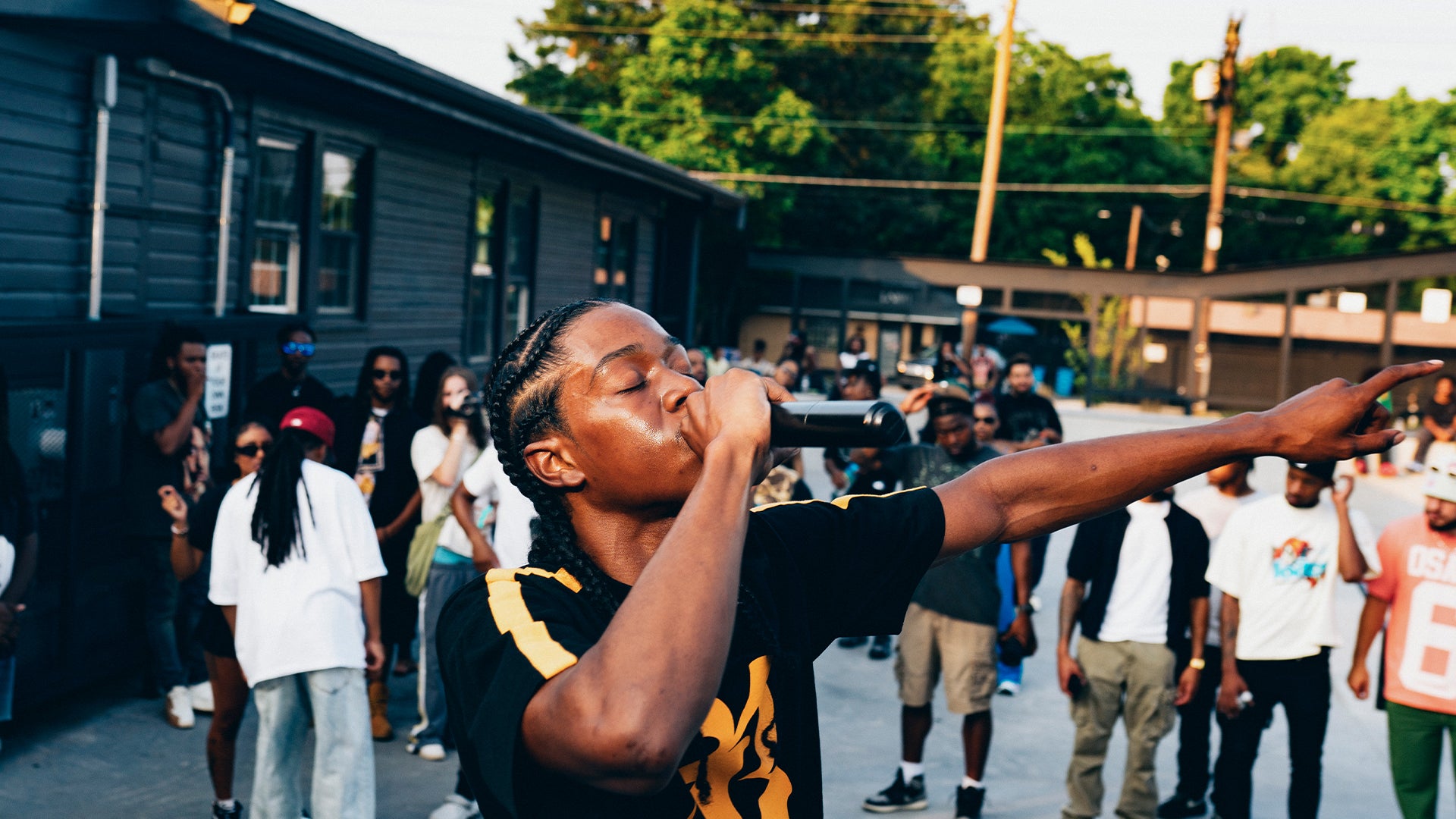 Man performing with microphone at outdoor streetwear event, crowd wearing trendy urban apparel