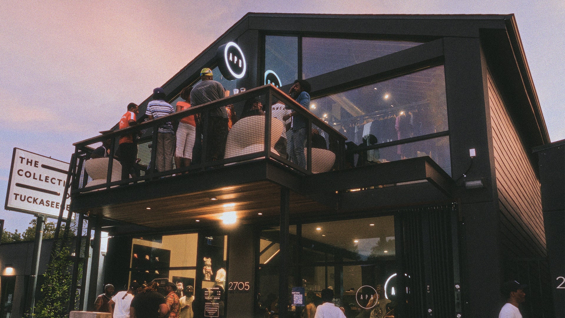 Modern streetwear store with glass facade, people gathering on balcony at dusk