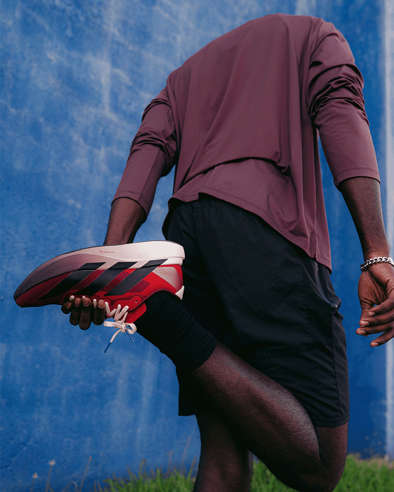 Man stretching in athletic streetwear, wearing red and black sneakers, against blue wall