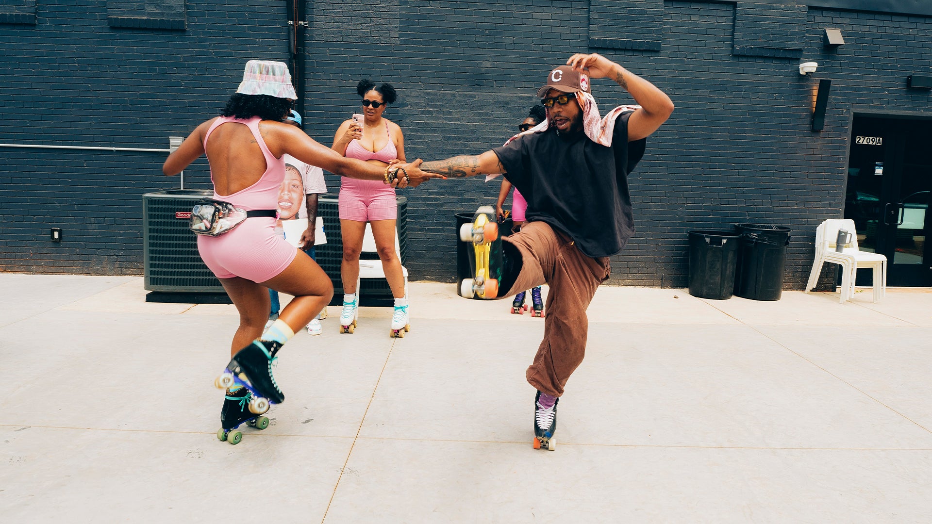 Group of people roller skating outdoors, two dancing in front, wearing streetwear apparel