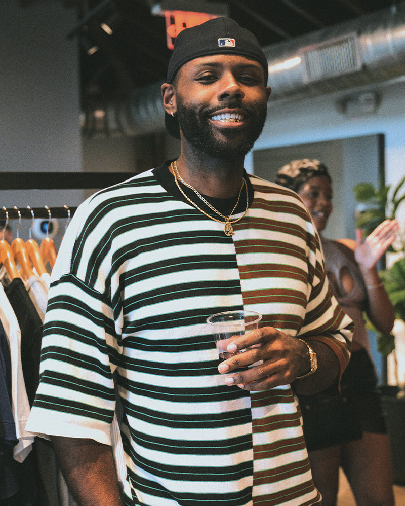 Man in a striped streetwear shirt and cap holding a drink at a clothing store event