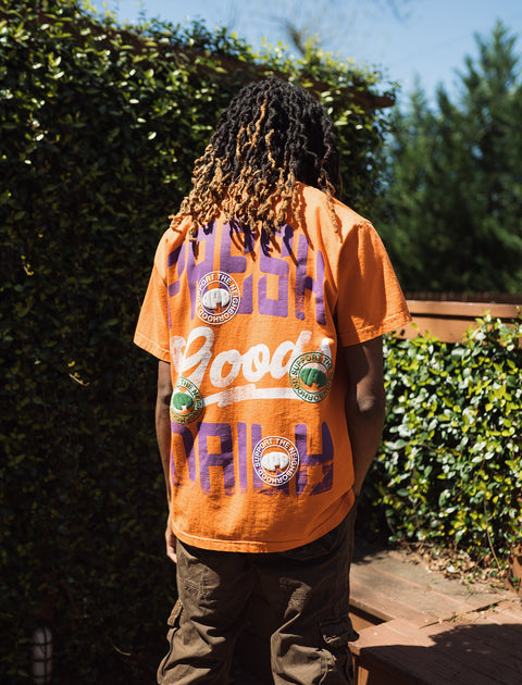 Man wearing orange graphic streetwear t-shirt with patches and cargo pants outdoors