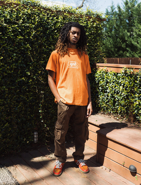 Man modeling orange graphic streetwear t-shirt, cargo pants, and sneakers outdoors