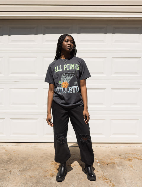 Woman wearing a graphic streetwear t-shirt, black ripped jeans, and boots outdoors