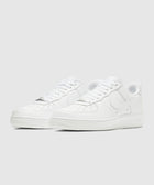 Pair of white low-top leather sneakers with perforated toe box and rubber soles on white background