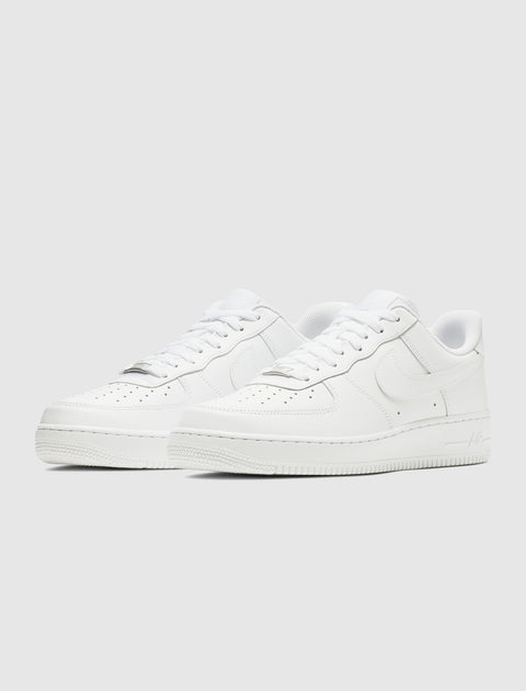 Pair of white low-top leather sneakers with perforated toe box and rubber soles on white background