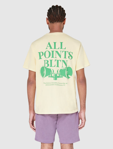 Back view of man wearing yellow graphic streetwear tee with green text and purple shorts