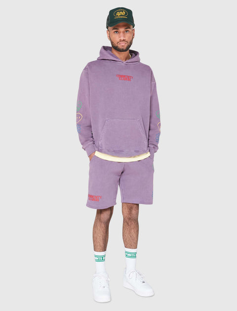 Man wearing purple hoodie and shorts set with 'Community Leaders' text, white sneakers, green cap