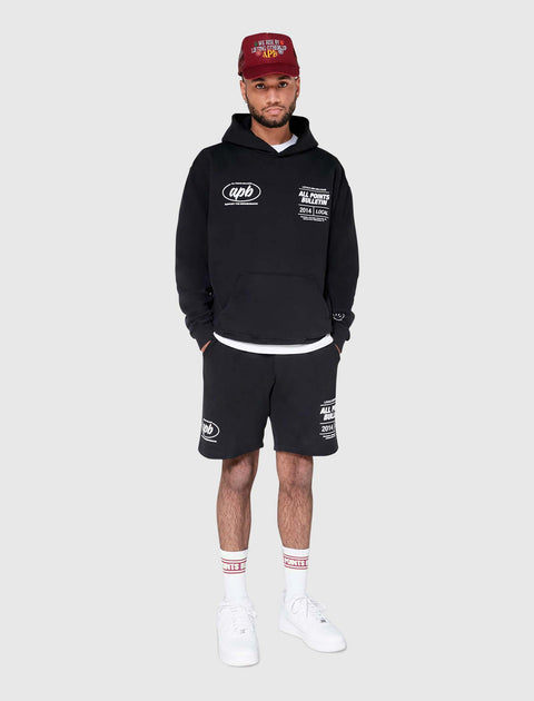 Man in black graphic hoodie and shorts set, maroon cap, white sneakers and socks